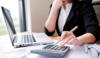 Accountant working on calculator with her laptop open and accounting paperwork