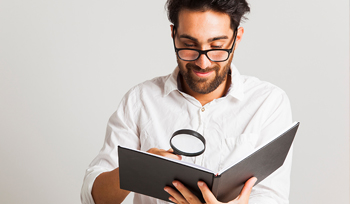 Male looking into a book with a magnifying glass